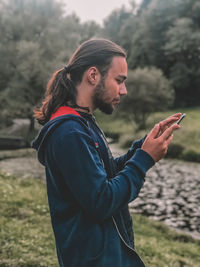 Side view of young man using phone while standing on field