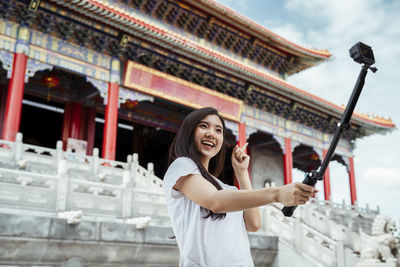 Smiling woman vlogging while standing against temple