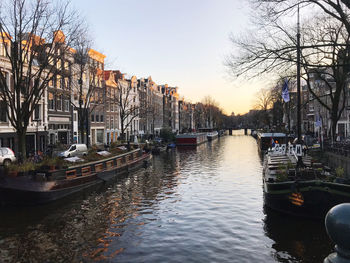 Sailboats moored in canal amidst buildings in city against sky