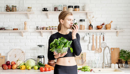 Young woman smelling avocado while standing in kitchen