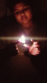 Young man holding lit candle in dark room