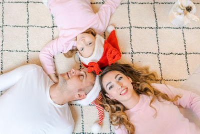 Family in santa hats with their daughter, in light, cozy clothes, lying