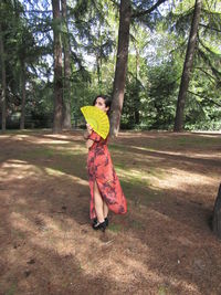 Full length of woman standing by tree in forest