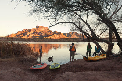 Friends with water sport equipment at lakeshore during dusk