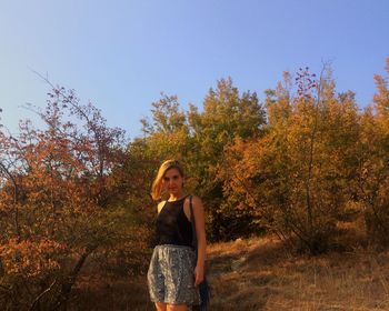 Portrait of beautiful young woman standing in forest against clear sky