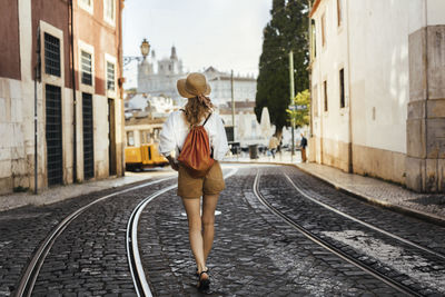 Rear view of woman walking on railroad tracks in city