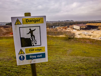 Warning sign on field against sky