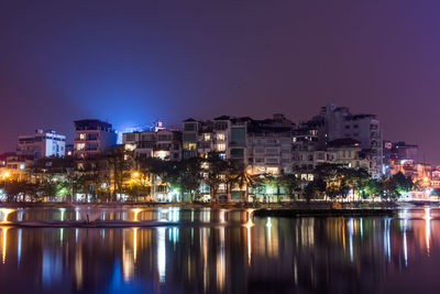 Illuminated buildings by sea against sky at night