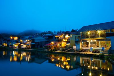 Illuminated buildings by river against sky at night