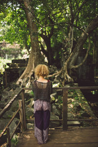 Rear view of mid adult woman with curly hair standing by railing against trees