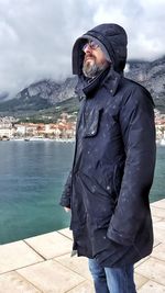 Man wearing warm clothing looking at view by lake during winter