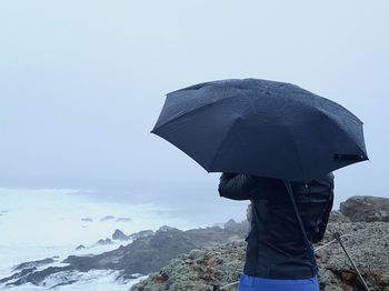 Midsection of woman holding umbrella on cliff during rain