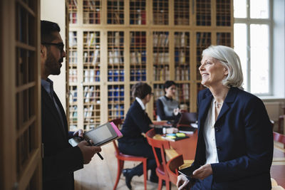 Happy senior professional discussing with coworker in board room at library