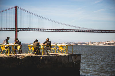 People on suspension bridge over sea against sky