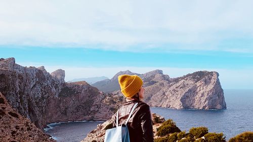 Rear view of woman with backpack looking at sea against cloudy sky