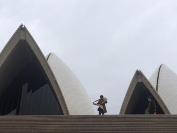 Low angle view of woman standing by building against sky