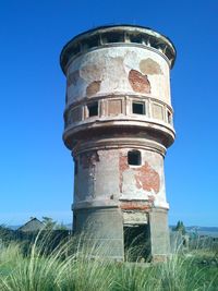 Low angle view of water tower on field against clear blue sky