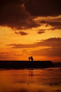 Silhouette people riding on sea against sky during sunset