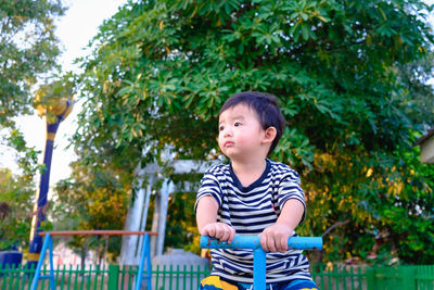 Boy looking away while sitting on seesaw in park against trees
