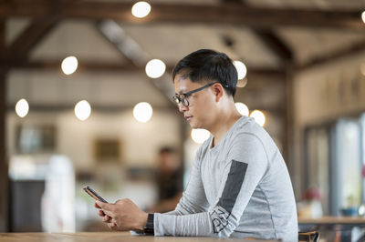 Side view of man using mobile phone sitting at cafe