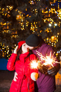 Woman holding umbrella standing in illuminated park during winter