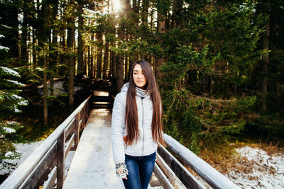 Woman standing on snowy footbridge in forest