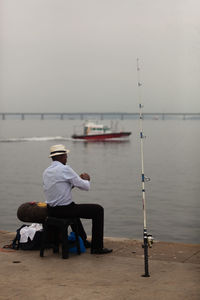 Rear view of man fishing in sea against sky
