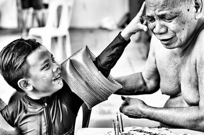 Boy applying cake on face of senior man