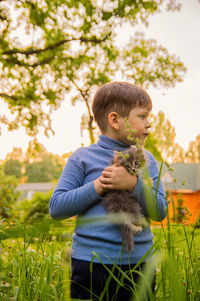 Cute boy holding cat looking away while standing outdoors