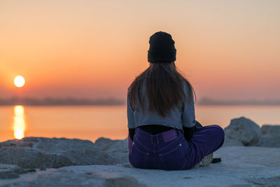 Rear view of woman sitting on beach during sunset