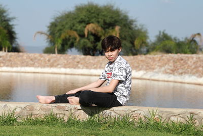 Boy sitting on lake against plants