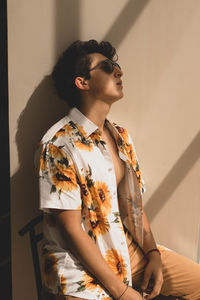 Man wearing sunglasses while sitting against wall