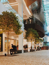 People sitting on street by modern buildings in city