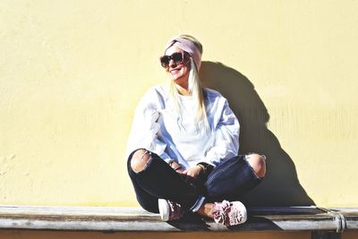 Young woman wearing sunglasses sitting on wall