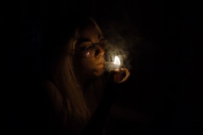 Close-up of woman igniting cigarette over black background