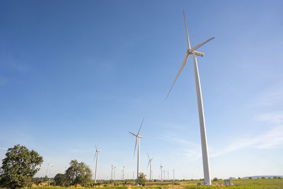 Low angle view of wind turbines on field against sky