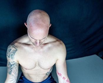 Shirtless bald man doing yoga against black background