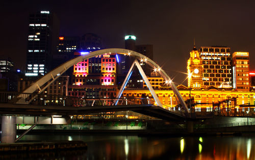 Illuminated bridge over river in city against sky at night