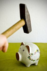 Close-up of person holding hammer over piggy bank