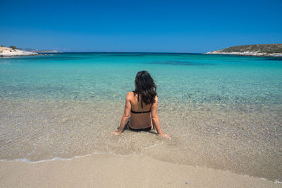 Rear view of woman wearing bikini sitting in sea