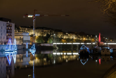 Illuminated city by river against sky at night