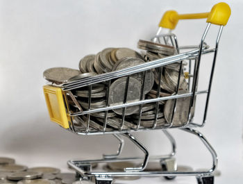 Close-up of coins in shopping cart against white background