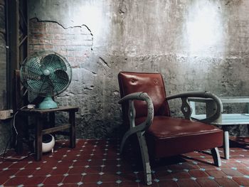 Empty armchair by electric fan in old room