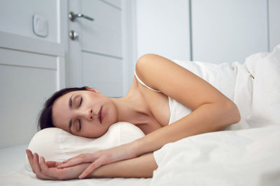 Woman in a white t-shirt is lying on the bed and a pillow is under the blanket in the room