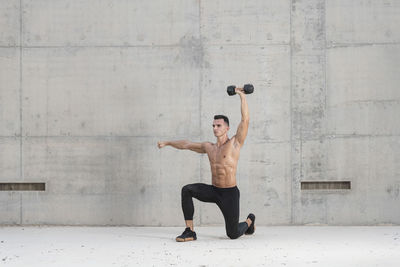 Full length of shirtless man with arms raised against wall