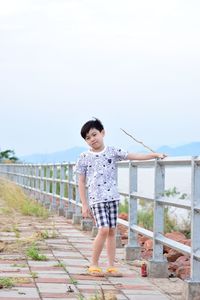Full length of boy standing by railing against sky