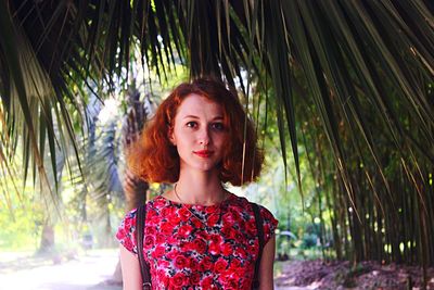 Portrait of young woman standing amidst palm leaves