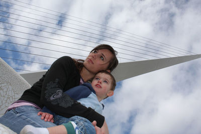 Low angle view of mother with son sitting at sundial bridge against cloudy sky