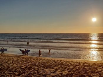 Silhouette people on beach against sky during sunset