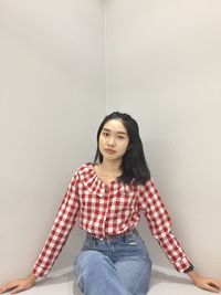 Portrait of young woman sitting against wall